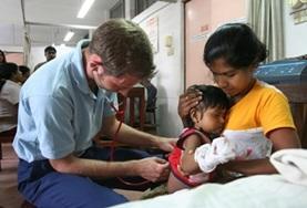 Projekte im Ausland - Sri Lanka : Medizin - Praktikum Ein Freiwilliger im Krankenpflegepraktikum in Sri Lanka untersucht ein Kind, das auf dem Schoß seiner Mutter sitzt.
