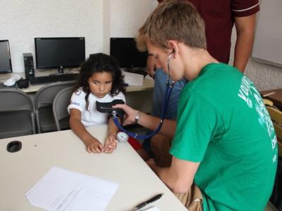 Ein Freiwilliger im Public Health Projekt misst den Blutdruck eines Kindes Ein Freiwilliger von Projects Abroad im Public Health Projekt misst den Blutdruck eines kleinen Mädchens