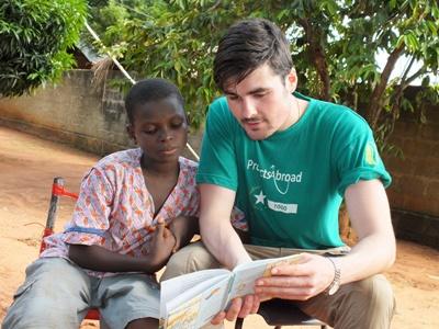 Ein Freiwilliger übt mit einem Kind im Gemeindezentrum das Lesen Im Schulferien – Special in Togo lernst du Französisch und kannst es sofort vor Ort anwenden
