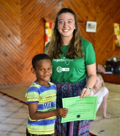 Freiwillige überreicht einem Schüler der Holiday School seine Abschluss-Urkunde Im Schulferien - Special Sozialarbeit und Englisch auf den Fidschi - Inselns