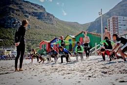 Freiwilligenarbeit in Afrika - Südafrika : Sport - Praktikum Freiwillige im Surf - Projekt bei Aufwärmübungen mit den Surfschüler/innen am Strand von Muizenberg.